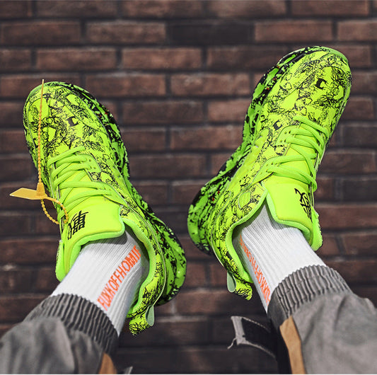 Bright green soccer cleats worn with gray pants and white socks against a brick wall.