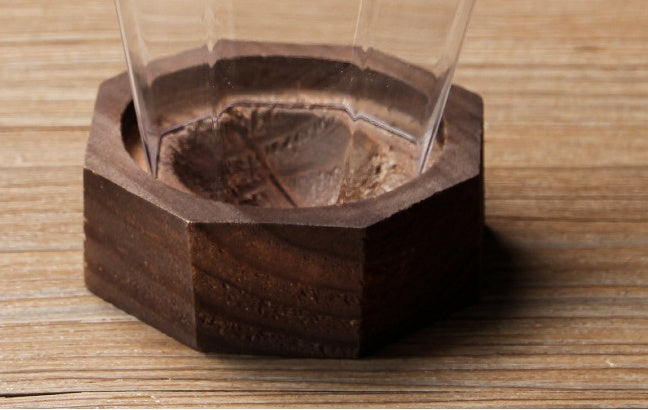 A hand holding a clear crystal wine glass with a wooden round base on a table, with ice cubes and a lime in the background.