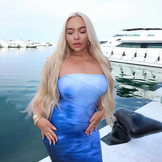 Woman in a blue strapless dress standing by a marina with yachts in the background