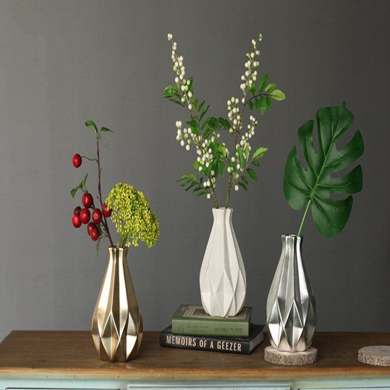 Three vases with decorative plants on a wooden surface against a gray wall