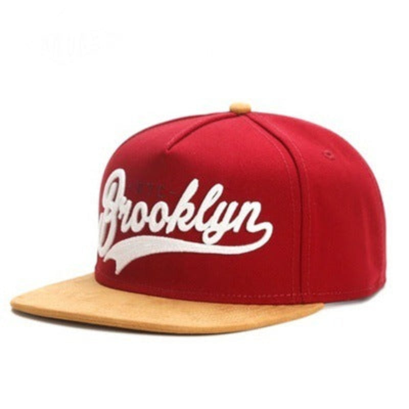 A red baseball cap with 'Brooklyn' embroidered in white on the front, featuring a short brim and a dome top style.