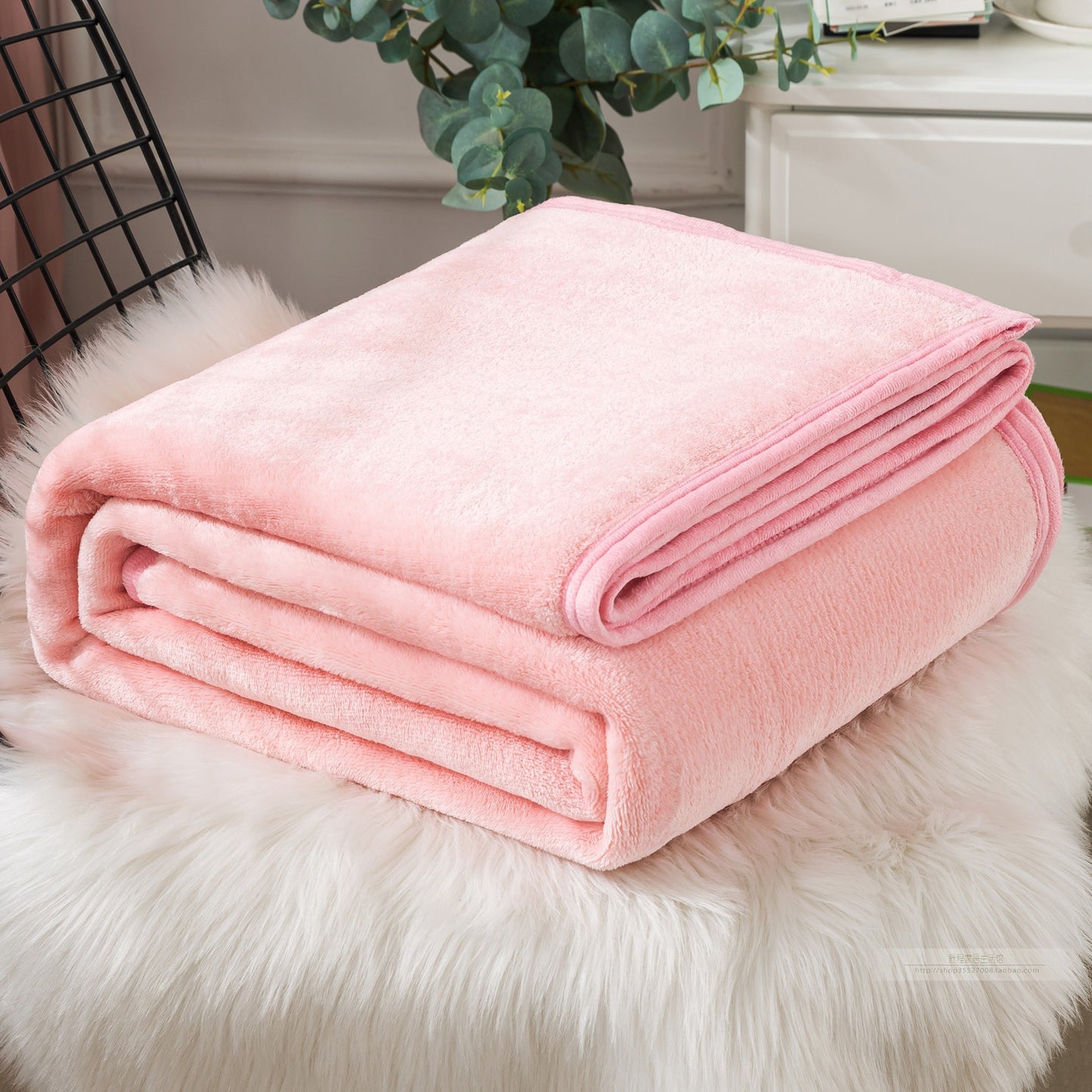 Pink blanket folded on a fluffy white surface with a decorative plant in the background.