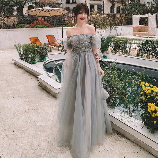 Woman in a light blue off-shoulder dress standing by a poolside with greenery and lounge chairs.