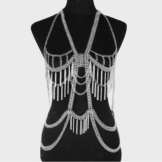 A gold-colored metal body chain displayed on a mannequin, featuring layered chains and fringe details.