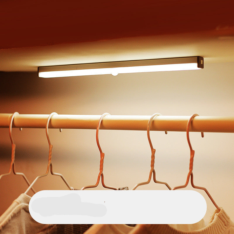 Under-cabinet LED light fixture above a clothing rack with hangers.