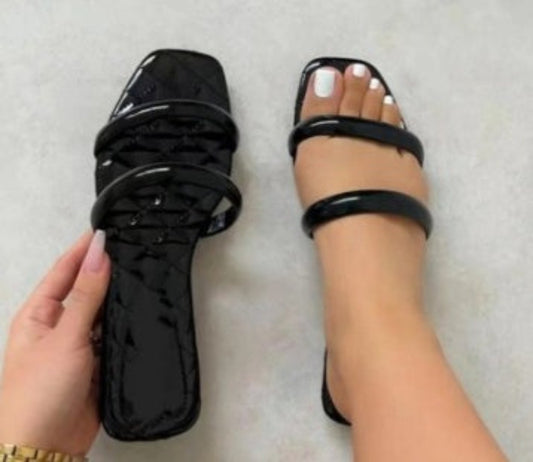 Black patent leather sandals being worn on a light gray background