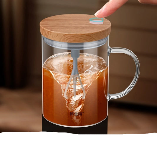 Glass mug with wooden lid and handle, filled with a brown liquid and a whisk, on a blurred background.