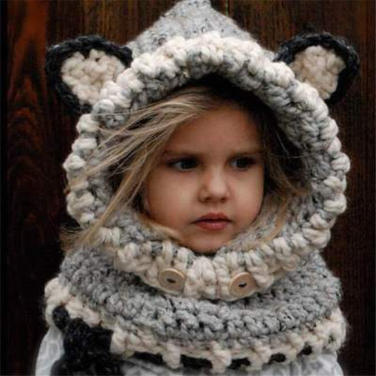 A baby wearing a beige knitted hat with a hood that has a bear face design and wooden button details.
