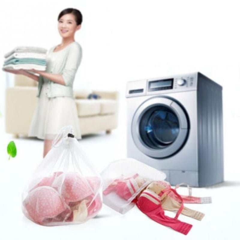 Woman holding clean clothes next to a washing machine with laundry bags on the floor.