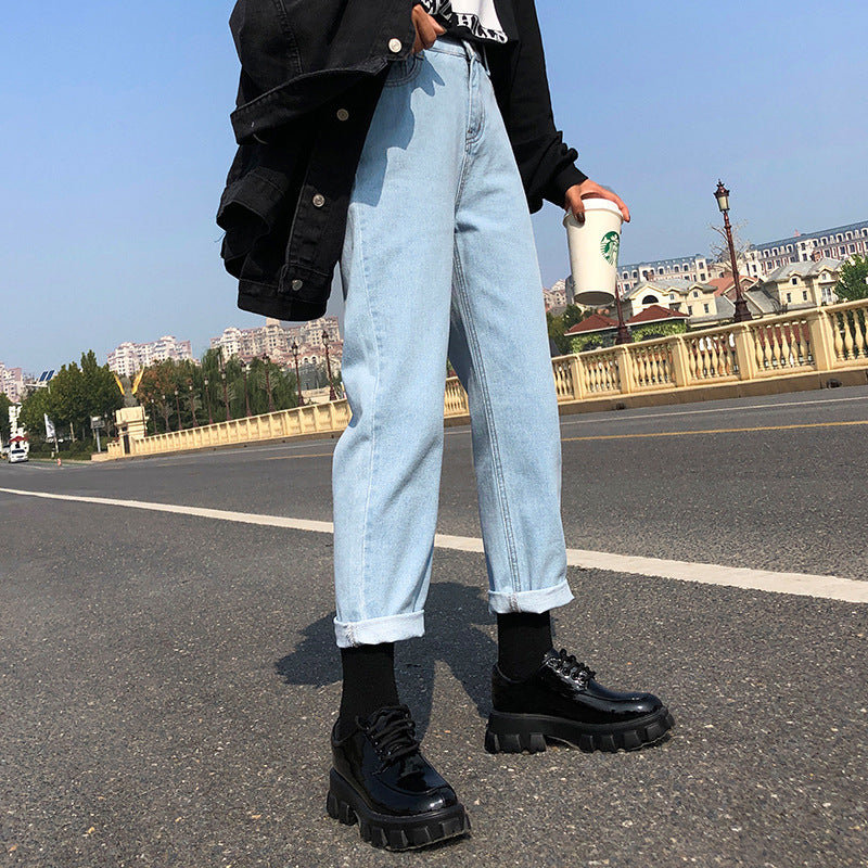 Person wearing light blue jeans and black shoes on a street with buildings in the background