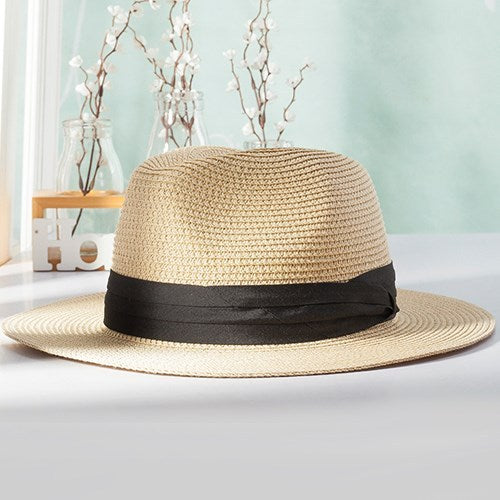 A beige panama hat with a black band placed on a flat surface, displayed against a light background with decorative items in the periphery.