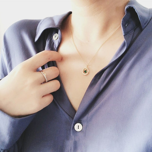 Person wearing a gold necklace with a green stone, adjusting it with a hand.