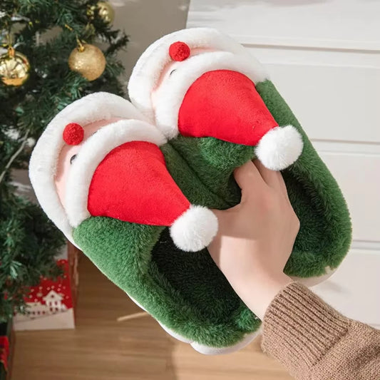 Green Christmas-themed slippers with red and white accents held in front of a decorated tree.