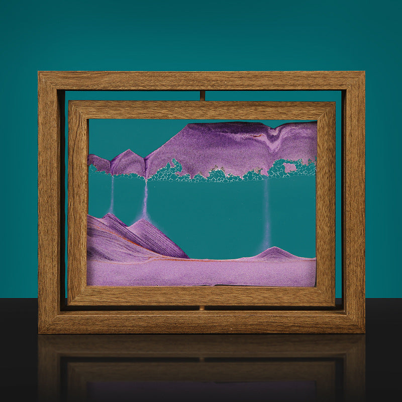 A framed glass decoration featuring a black and white mountain range with a blue water-like texture on the top half, set against a teal background.
