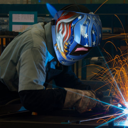 Person welding with a protective helmet featuring an American flag design, surrounded by sparks.