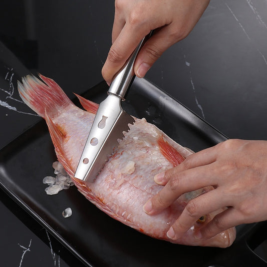 Person using a metal tool to clean a fish on a black surface