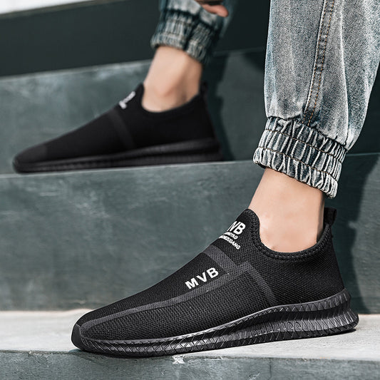 Black slip-on sneakers with 'MVB' branding worn by a person sitting on steps.