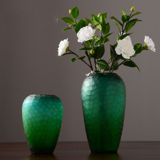 Two green vases with textured surface, one holding white flowers against a dark background