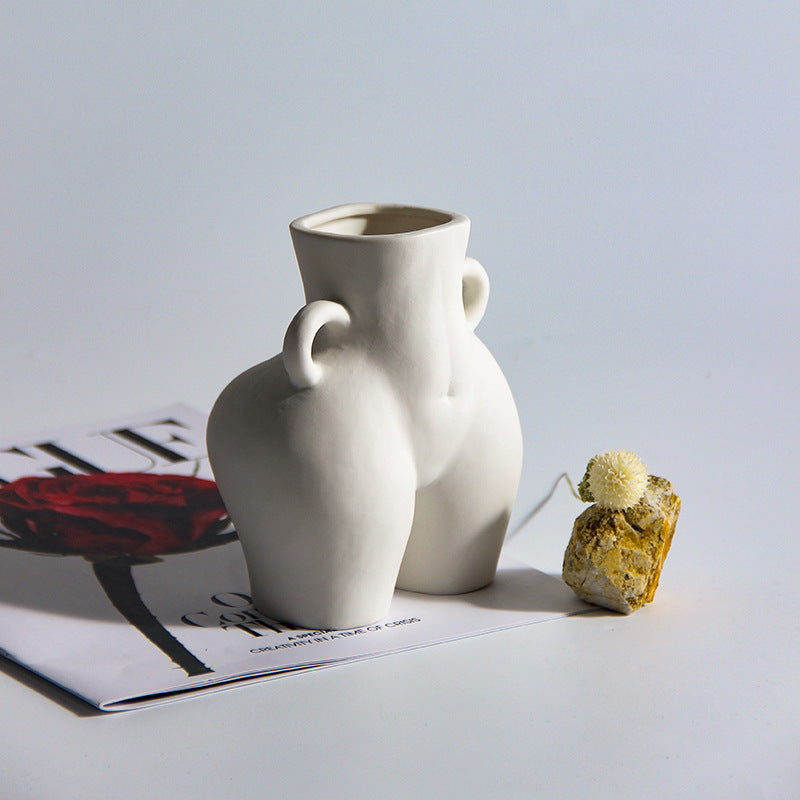A black ceramic gourd-shaped vase on a white surface, with a bouquet of multicolored flowers arranged in it, placed against a neutral background with a grey sofa.