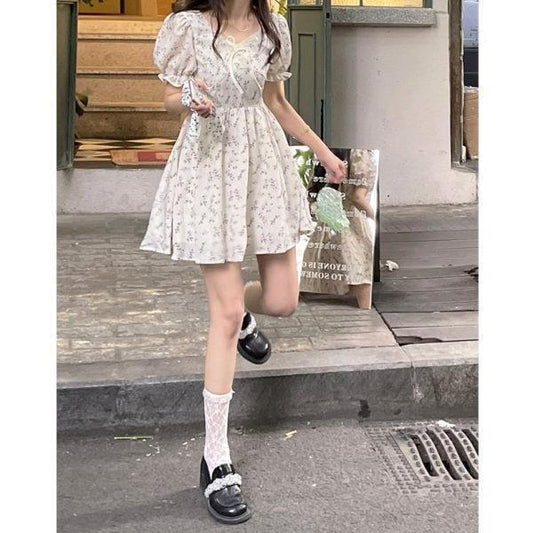 Woman in a floral dress and black shoes standing on a street.