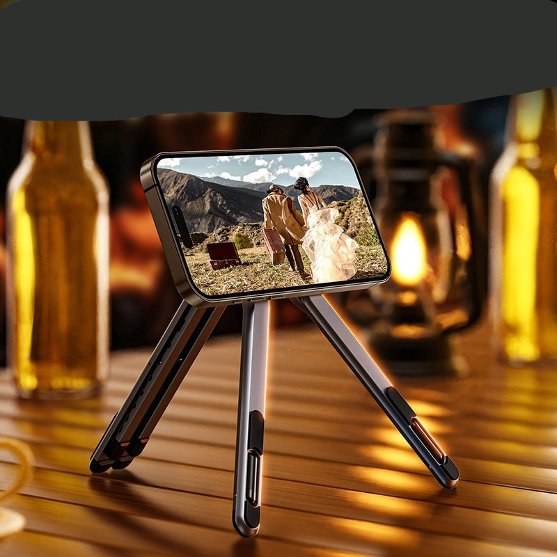 Phone stand on a wooden table with a scenic phone screen, surrounded by bottles and a lantern.