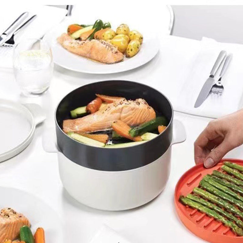 Cooking pot with salmon and vegetables on a table with a plate of food in the background.