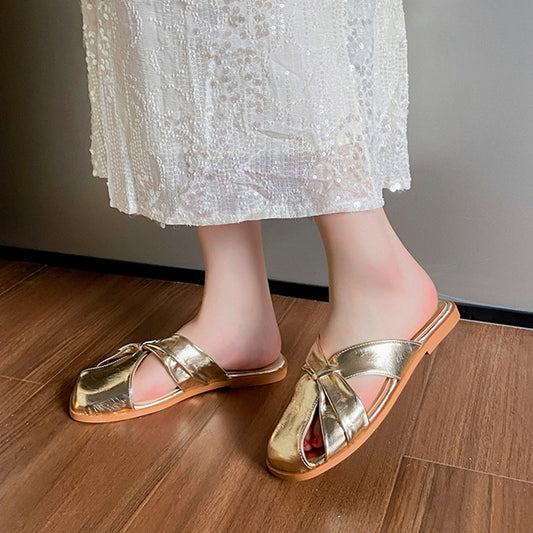 Gold sandals worn with a white lace skirt on a wooden floor.