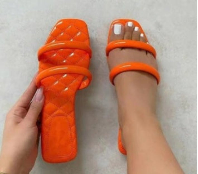 Orange quilted sandals held by a hand on a light gray background