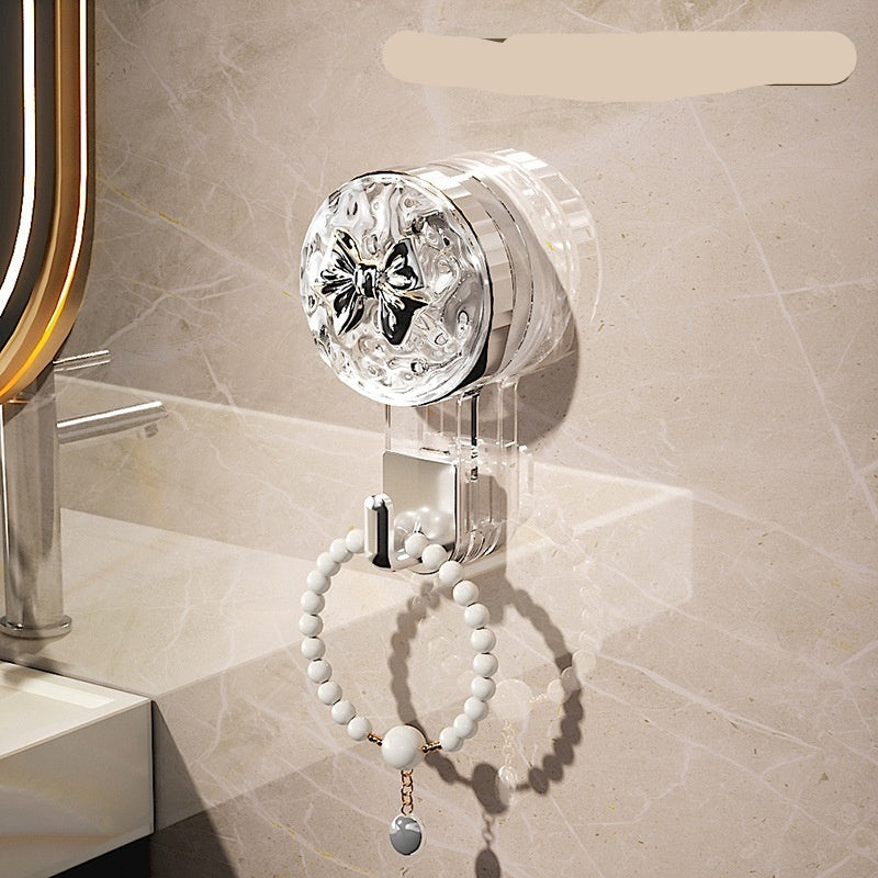 Transparent hook with silver bow on a bathroom wall, holding a bracelet.