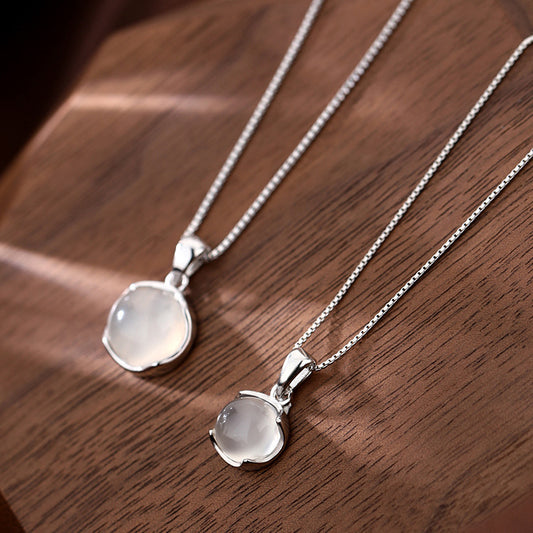 Two silver necklaces with round pendants on a wooden surface