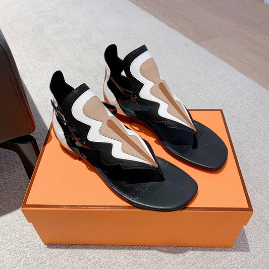 Black and white sandals with brown accents on an orange box