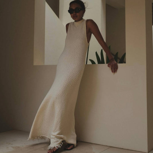 Woman in a white textured dress standing against a neutral wall.