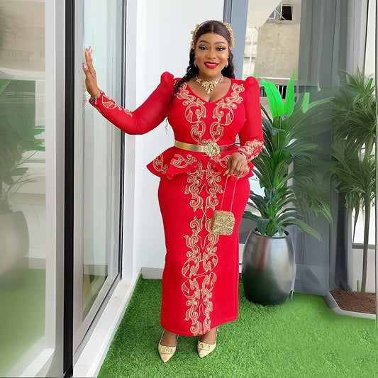 Woman in a red dress with gold embroidery standing in a modern indoor setting.