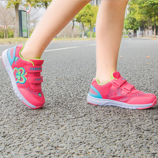 Pink children's sneakers with floral designs on a road.
