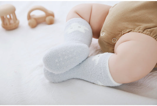 Baby's legs wearing white socks on a white surface with toys in the background