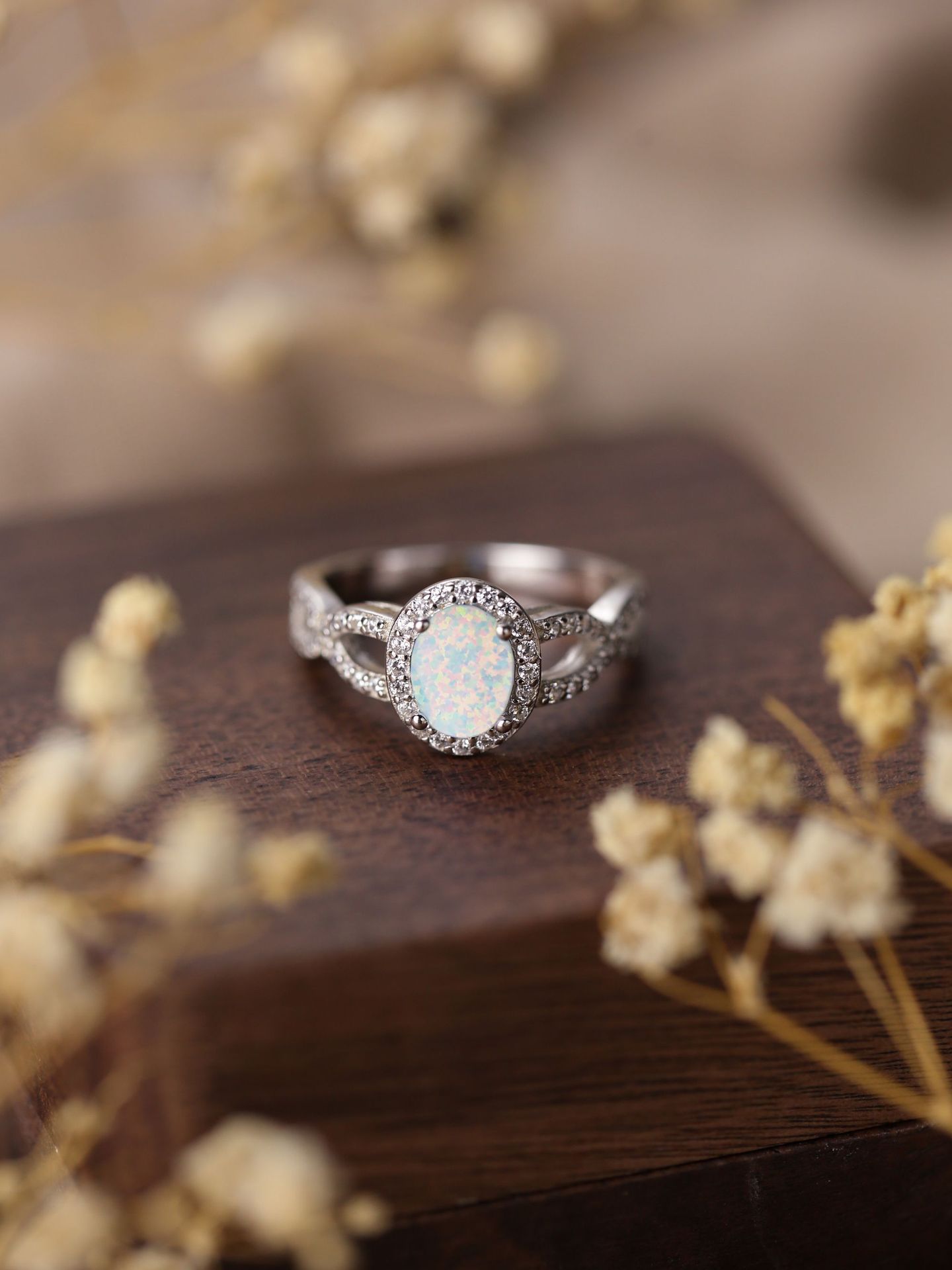 Silver ring with a central gemstone on a wooden surface with dried flowers.