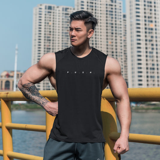 Man wearing a black sleeveless shirt with 'PUSH' text, standing by a waterfront with buildings in the background.