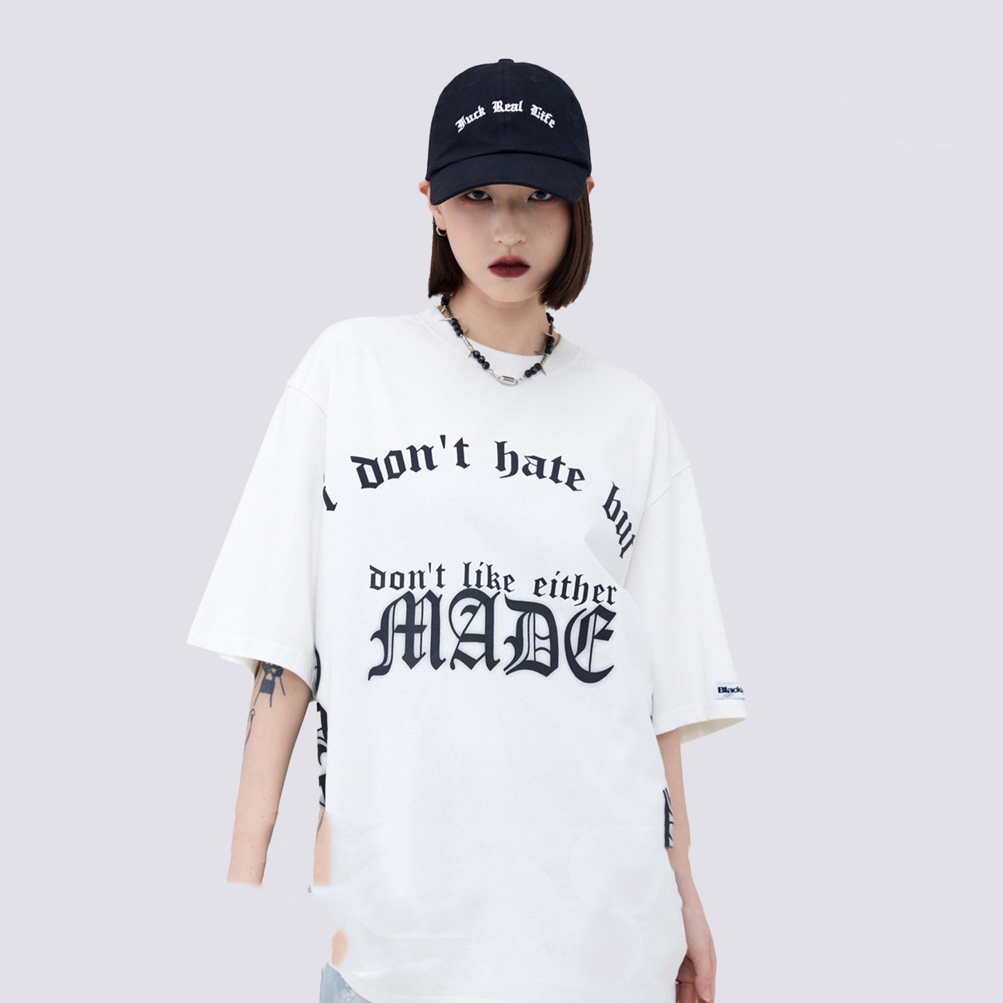 Person wearing a white t-shirt with text and a black cap on a light gray background