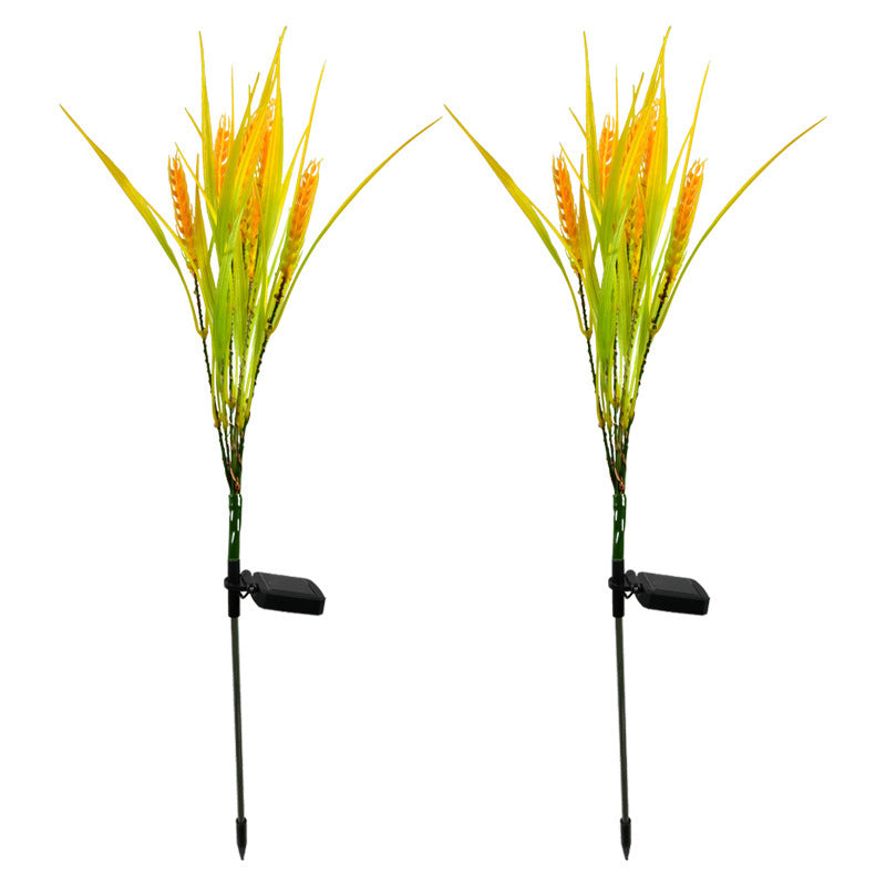 Two artificial grass plants with yellow spikes on black stakes against a white background
