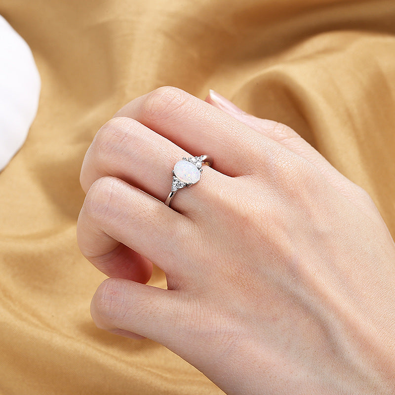 Hand wearing a silver ring with a heart-shaped gemstone on a beige fabric background
