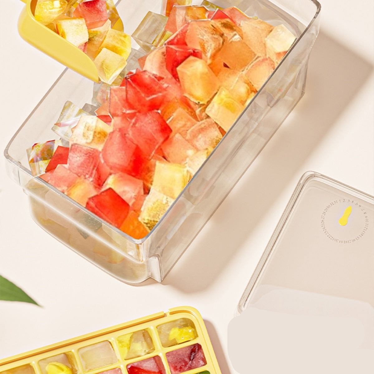 Colorful ice cubes in a container with an ice cube tray and scoop on a light surface.