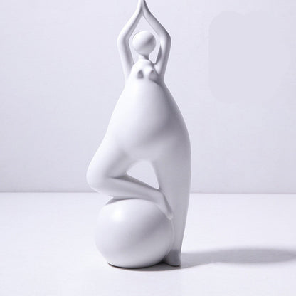 A pair of white ceramic figurines, one sitting and one standing, placed on top of a stack of books with a decorative vase beside them.