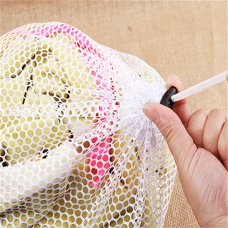 Hand holding a white mesh laundry bag with colorful spots on a beige background
