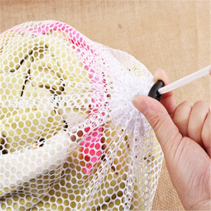 Hand holding a white mesh laundry bag with colorful spots on a beige background