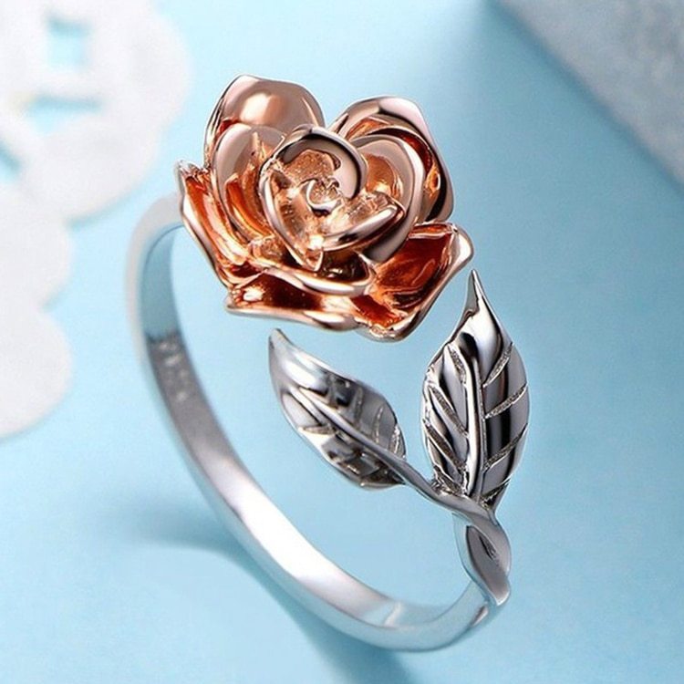 Rose gold and silver rose-shaped ring on a light blue background