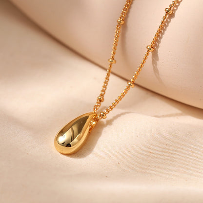 Gold necklace with a teardrop pendant on a beige fabric background