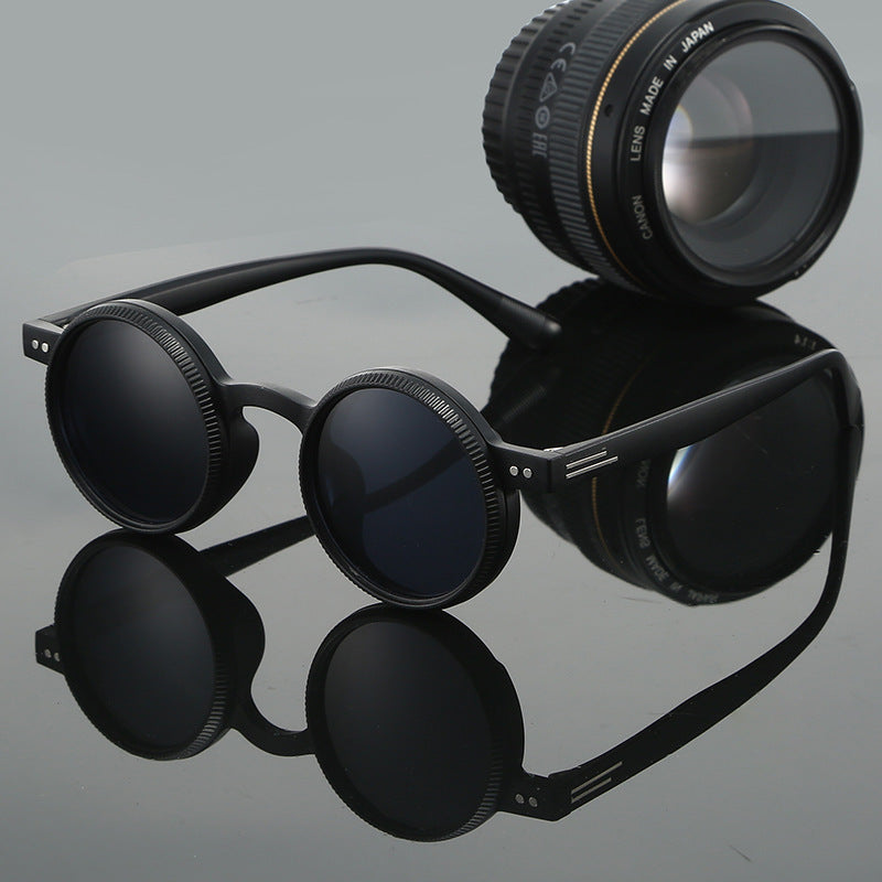 Black sunglasses with a camera lens on a reflective gray surface