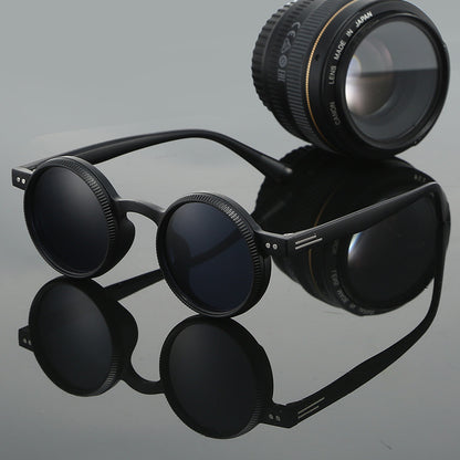 Black sunglasses with a camera lens on a reflective gray surface