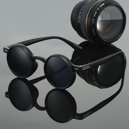 Black sunglasses with a camera lens on a reflective gray surface