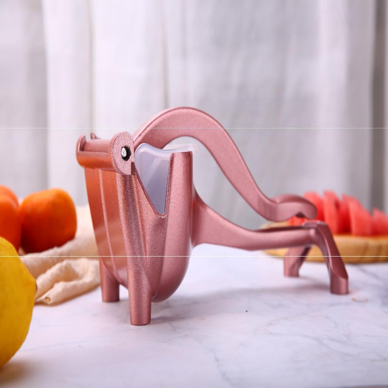 Pink dinosaur-shaped fruit peeler on a white surface with fruits in the background